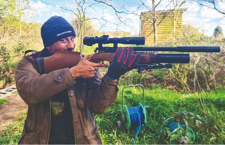 A man shooting an air rifle and smiling towards the camera