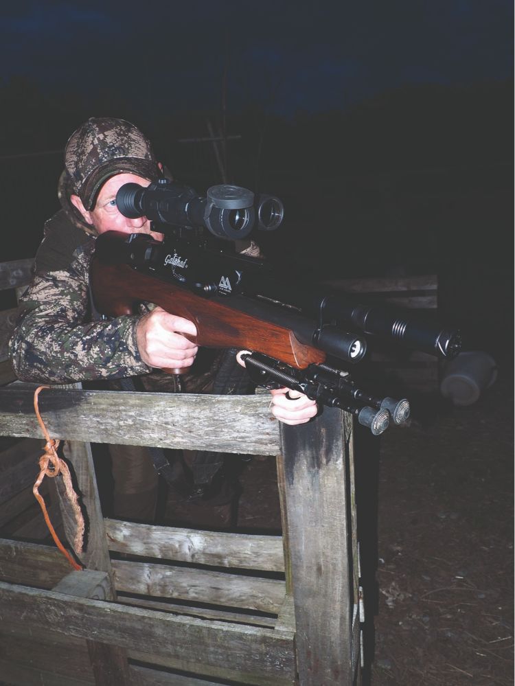 A man shooting an air rifle out of the window of a car using a thermal scope